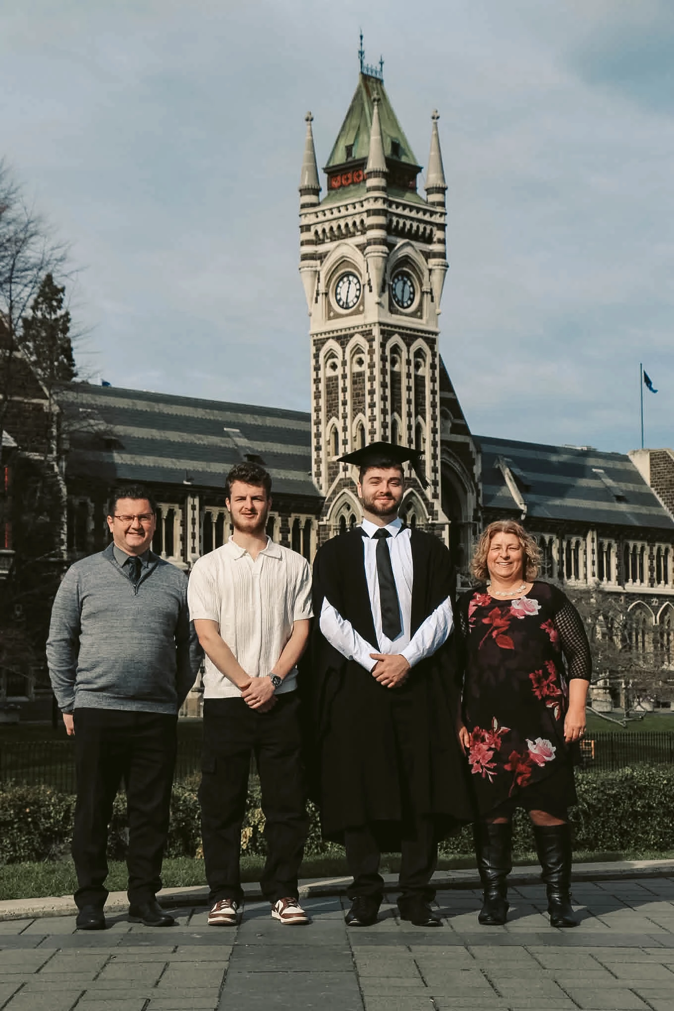 Graduate standing with family beneath the Dunedin clock tower
