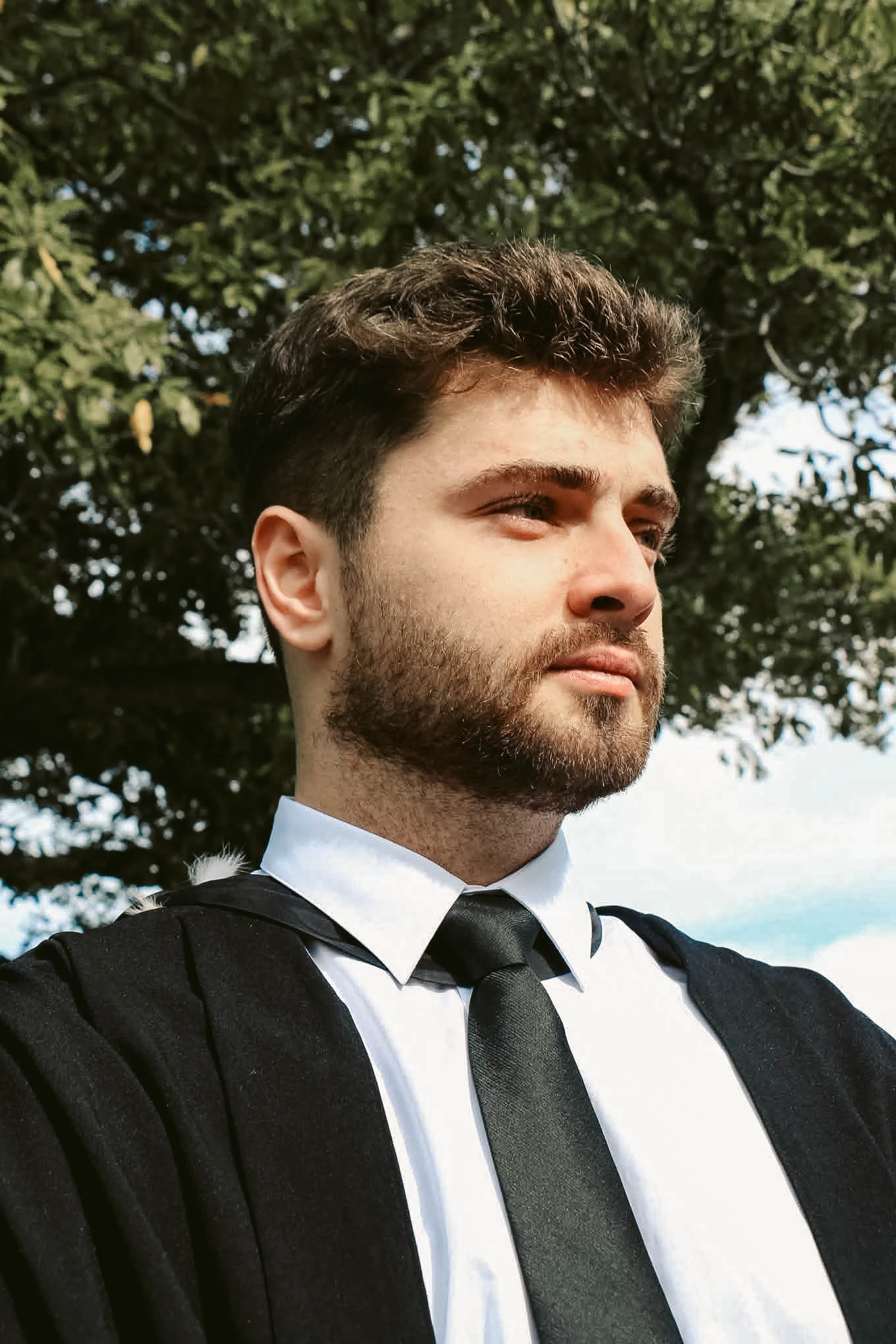 Close portrait of a graduate in formal dress beneath trees